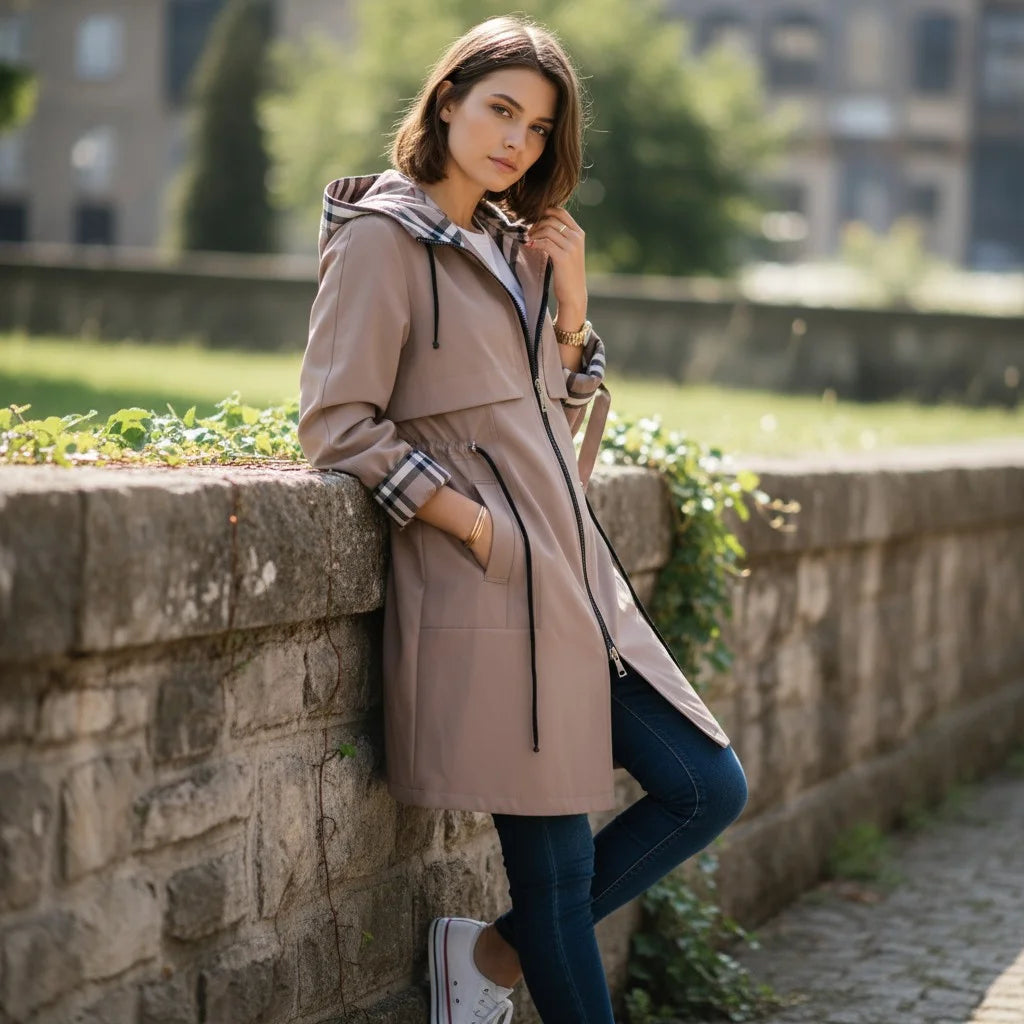 Woman in a beige coat leaning against a stone wall outdoors
